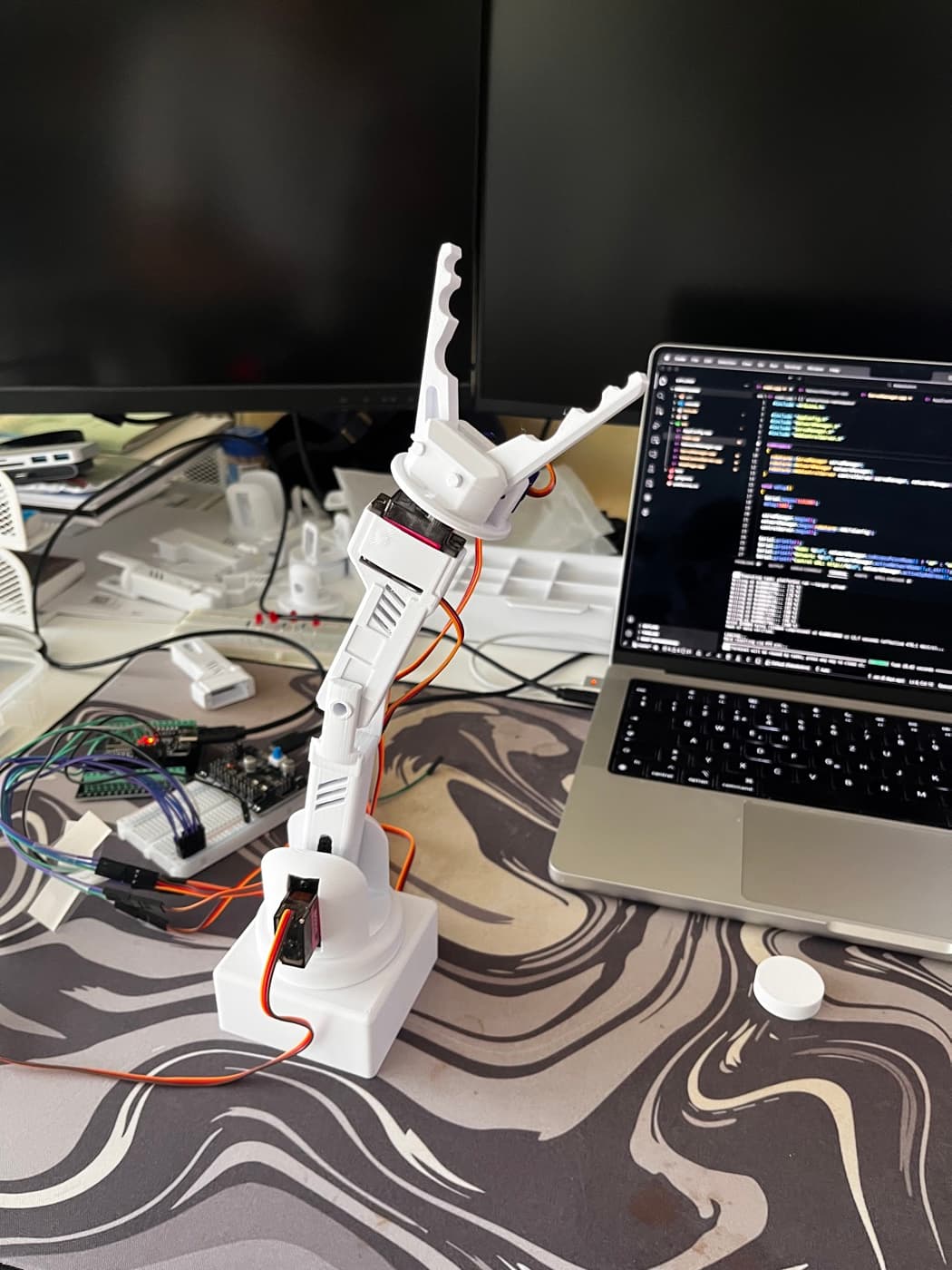 Der kleine selbst gebaute Roboterarm mit Mikroservos, daneben ein Laptop mit dem Code dazu.