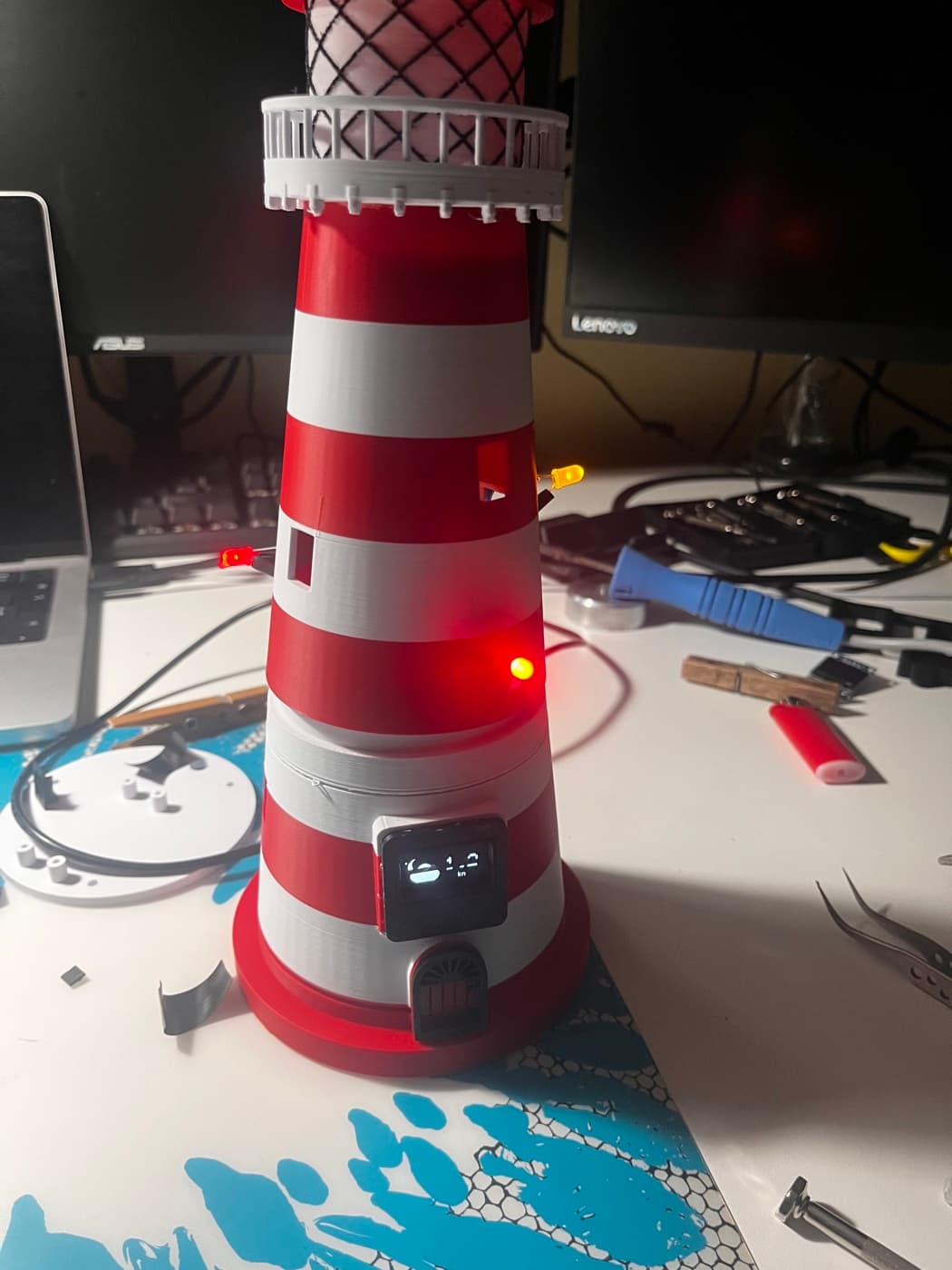 Der Leuchtturm auf der Werkbank, die Fenster-LEDs leuchten rot und orange.